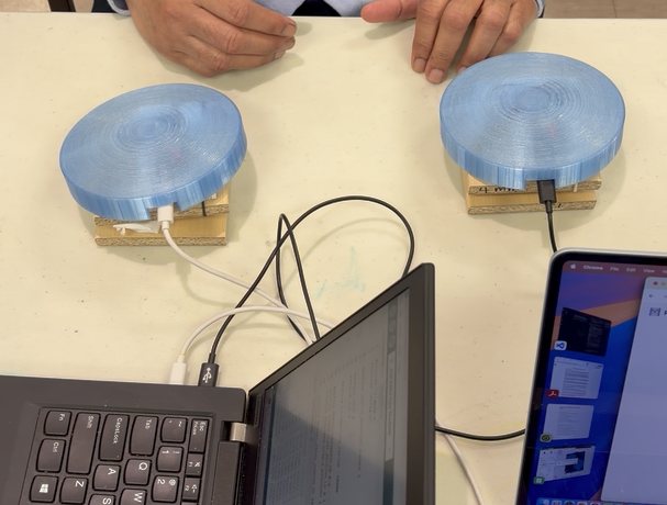 Two prototype ReclaiMove tiles with translucent blue domes on a table, a participant resting their hands behind them.
